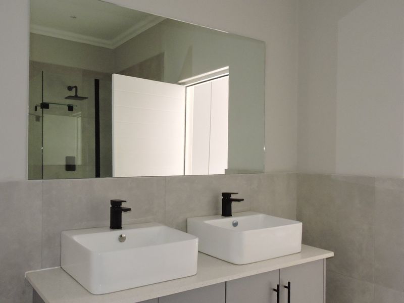 Modern bathroom featuring a double vanity with vessel sinks, black mixer taps, a large wall mirror, and a glass shower enclosure.