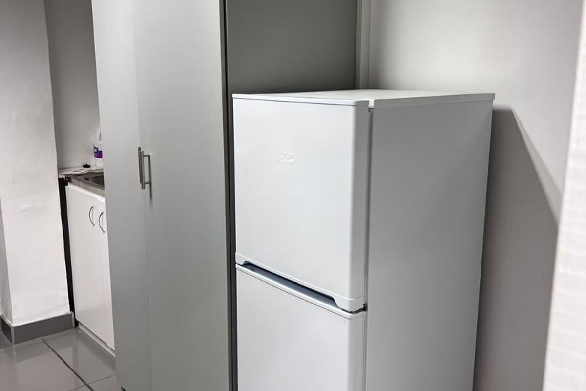 A compact kitchenette area featuring built-in cabinetry and tiled flooring, suitable for office utility use.