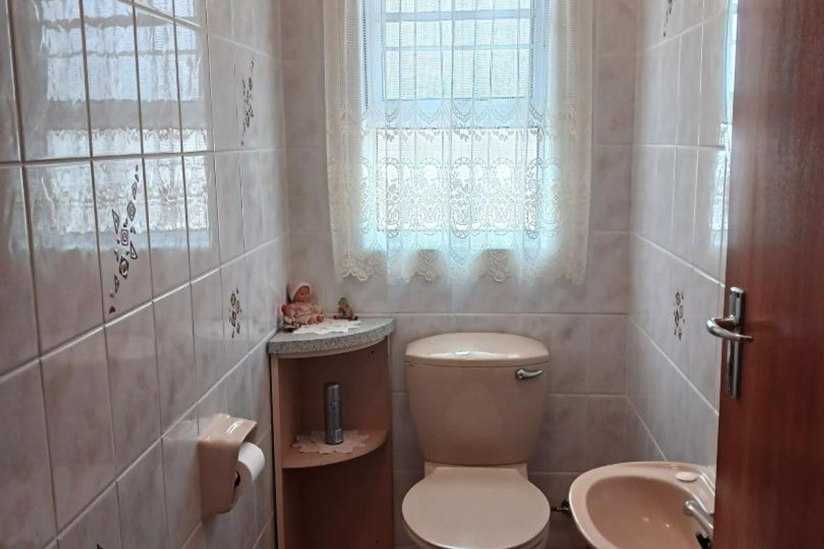 A compact guest bathroom featuring tiled walls, a standard toilet, and a wall-mounted basin with built-in corner storage.