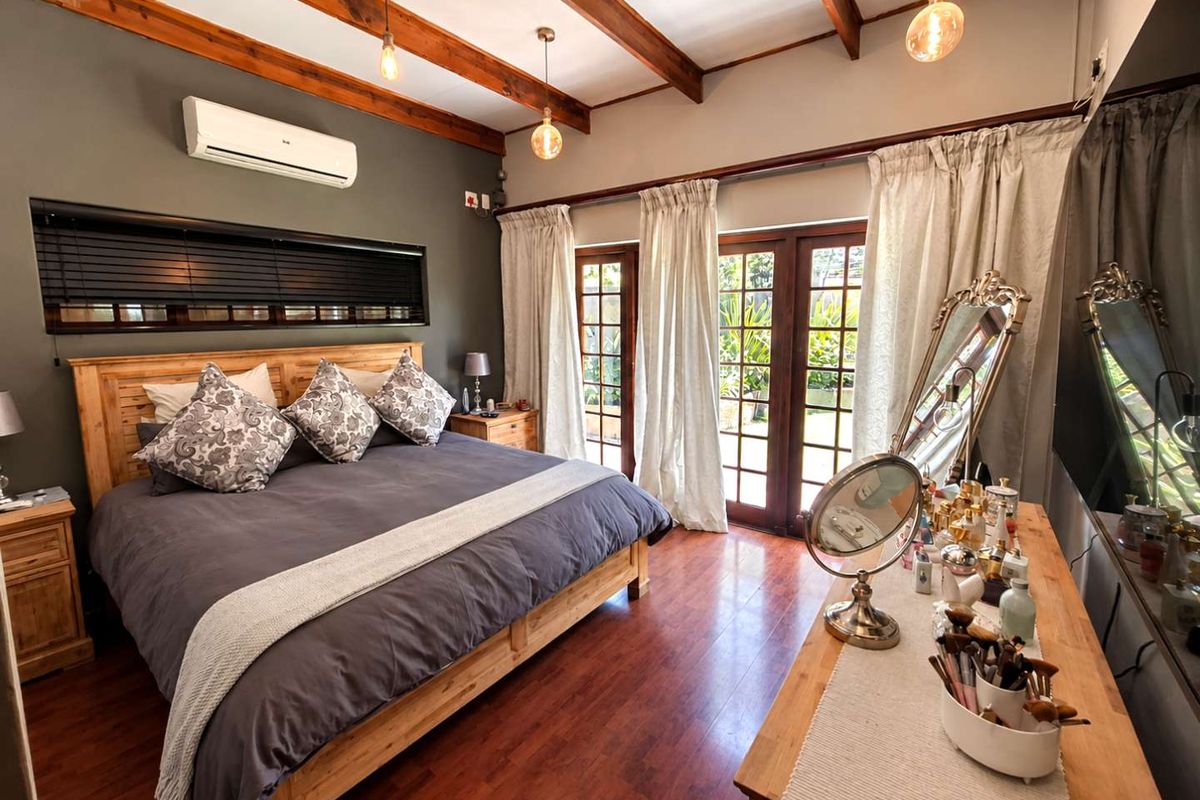 Spacious bedroom featuring exposed timber ceiling beams, laminate flooring, and direct access to the garden through timber-framed glass double doors.