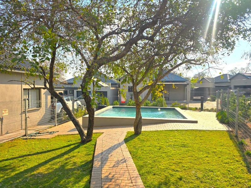 A well-maintained outdoor pool area featuring a paved walkway, established trees, and secure mesh fencing within a residential setting.