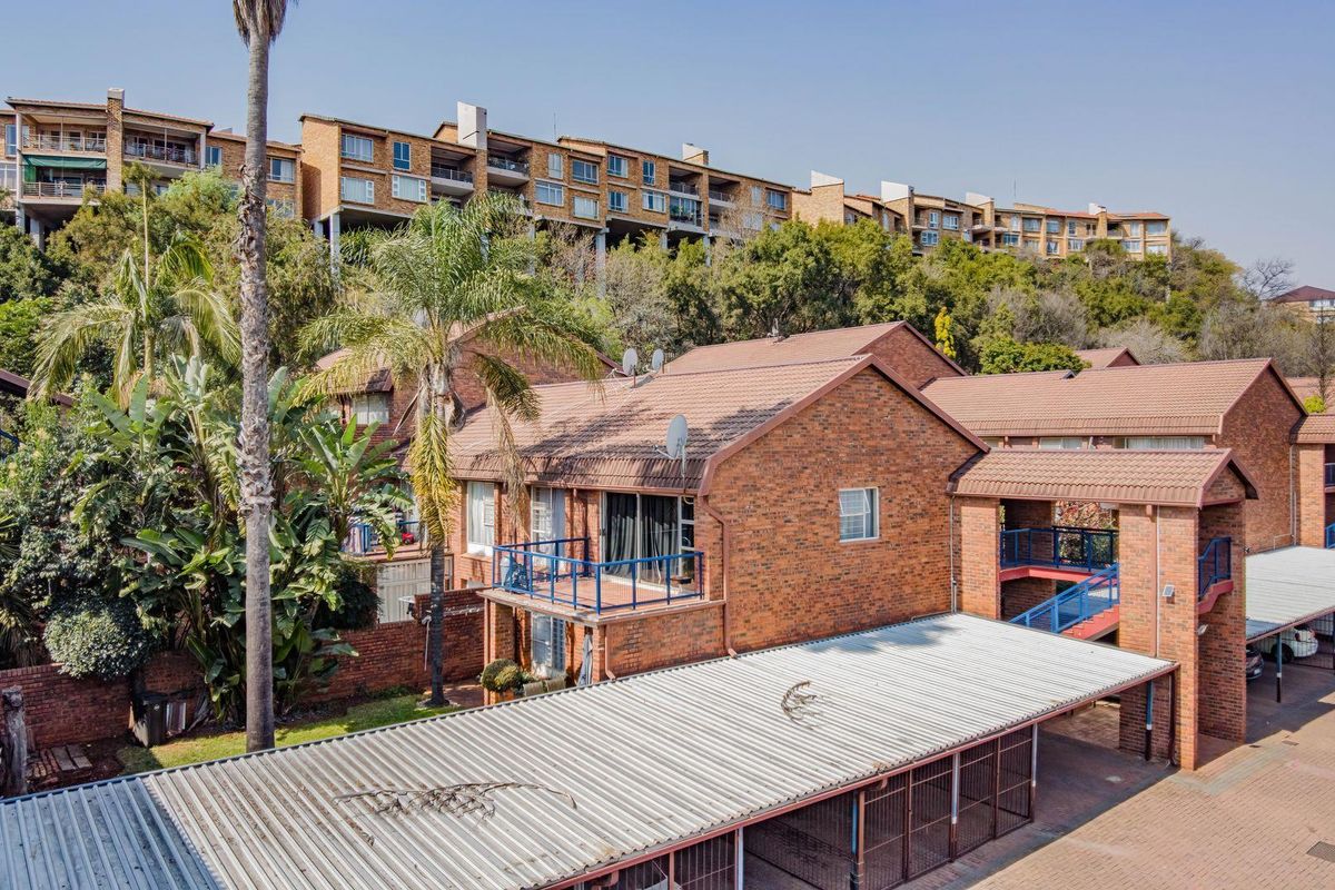 An elevated view of the apartment complex featuring brick exterior walls, tiled roofing, a private balcony, and covered carport parking facilities.