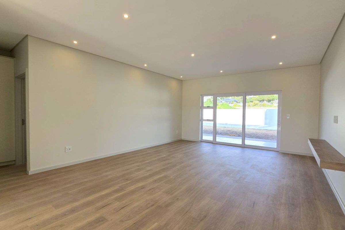 A bright, modern, and empty living room featuring light wood-look laminate flooring, recessed downlights, a built-in cupboard, and a sliding door leading outdoors.