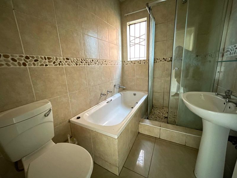 A functional bathroom featuring a built-in bathtub, separate glass shower enclosure, and pedestal basin with neutral ceramic tiling throughout.