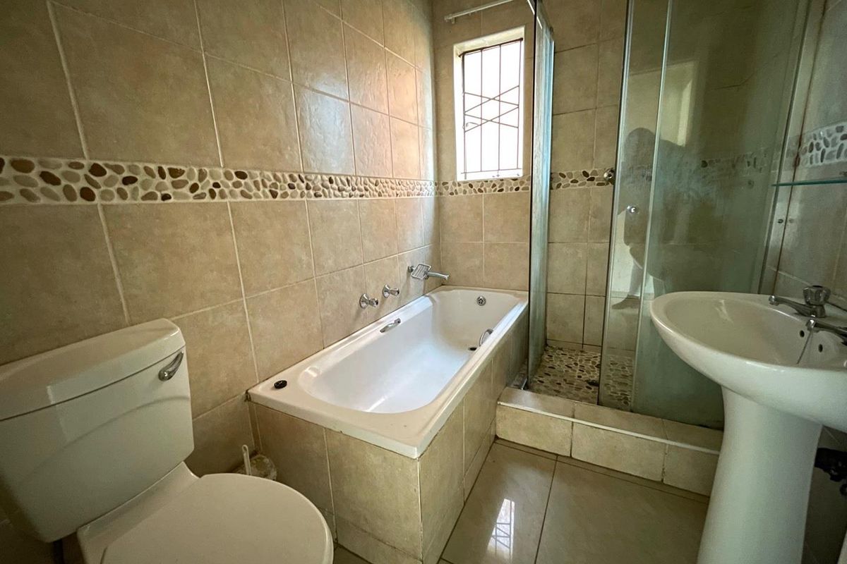 A functional bathroom featuring a built-in bathtub, separate glass shower enclosure, and pedestal basin with neutral ceramic tiling throughout.
