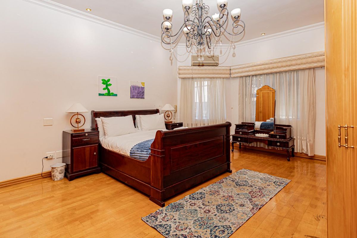 Spacious bedroom featuring polished hardwood flooring, built-in cabinetry, a decorative chandelier, and a wall-mounted air conditioning unit.