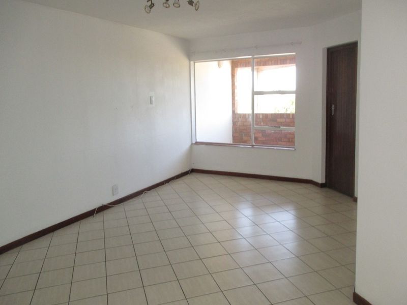 An empty, neutrally finished living area featuring tiled flooring, a ceiling light fixture, and a large window providing natural light.