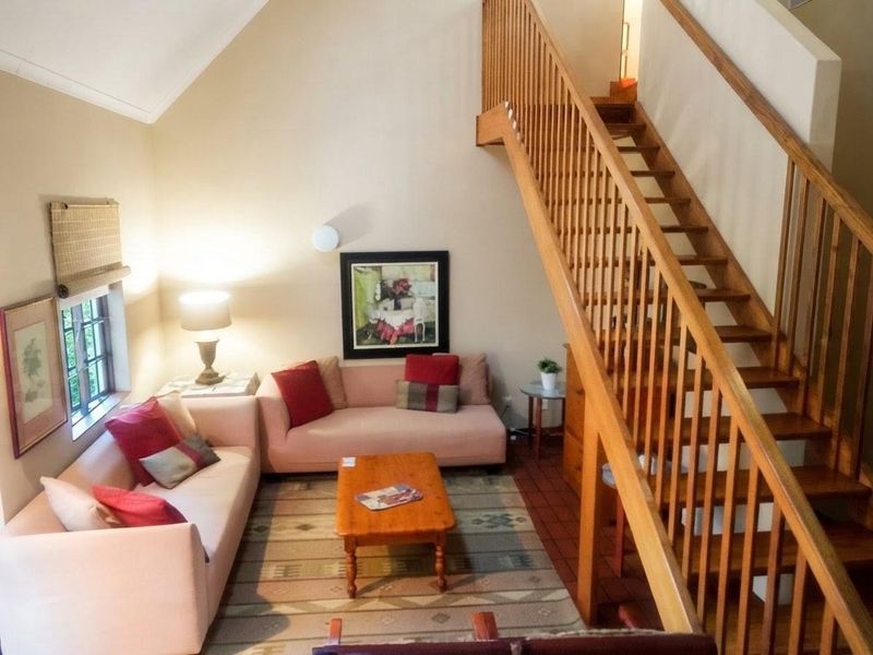 A cozy living room featuring a vaulted ceiling, tiled flooring, and a prominent wooden staircase with a matching balustrade.