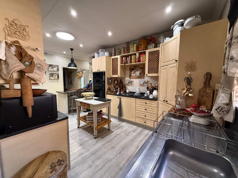 A functional kitchen featuring light wood cabinetry, dark countertops, integrated appliances, and recessed lighting, offering a warm and traditional aesthetic.