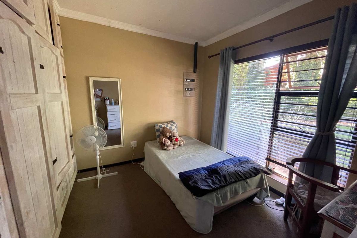 A bedroom featuring built-in wooden cupboards, carpeted flooring, and a large window with venetian blinds, providing natural light.