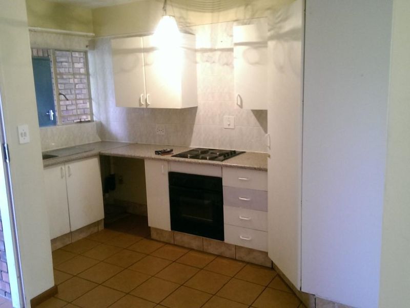 A functional kitchen featuring built-in cabinetry, an electric hob, an oven, and tiled flooring, offering a practical layout ready for modern updates.
