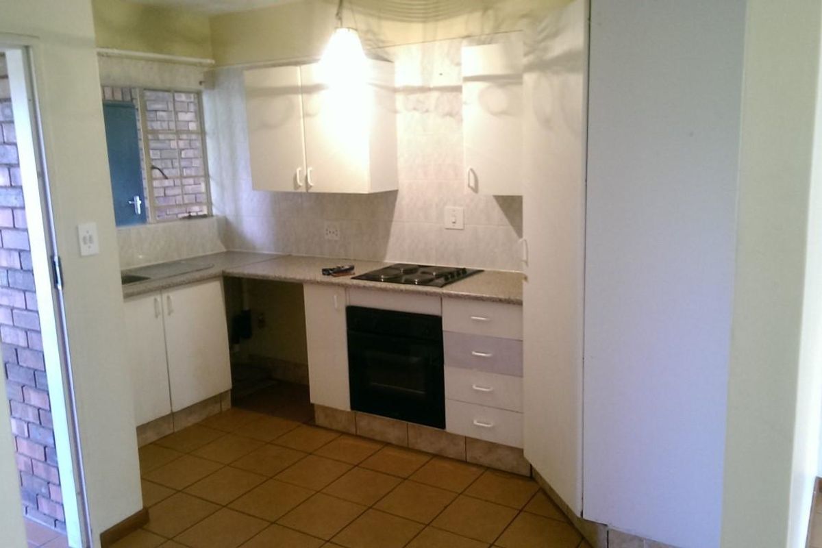 A functional kitchen featuring built-in cabinetry, an electric hob, an oven, and tiled flooring, offering a practical layout ready for modern updates.
