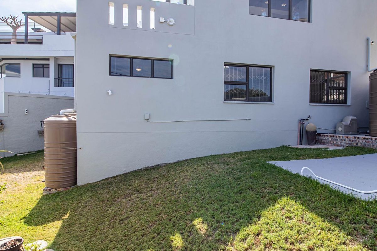 Rear exterior view of the property featuring a landscaped lawn, two water storage tanks, and a paved area adjacent to the building facade.