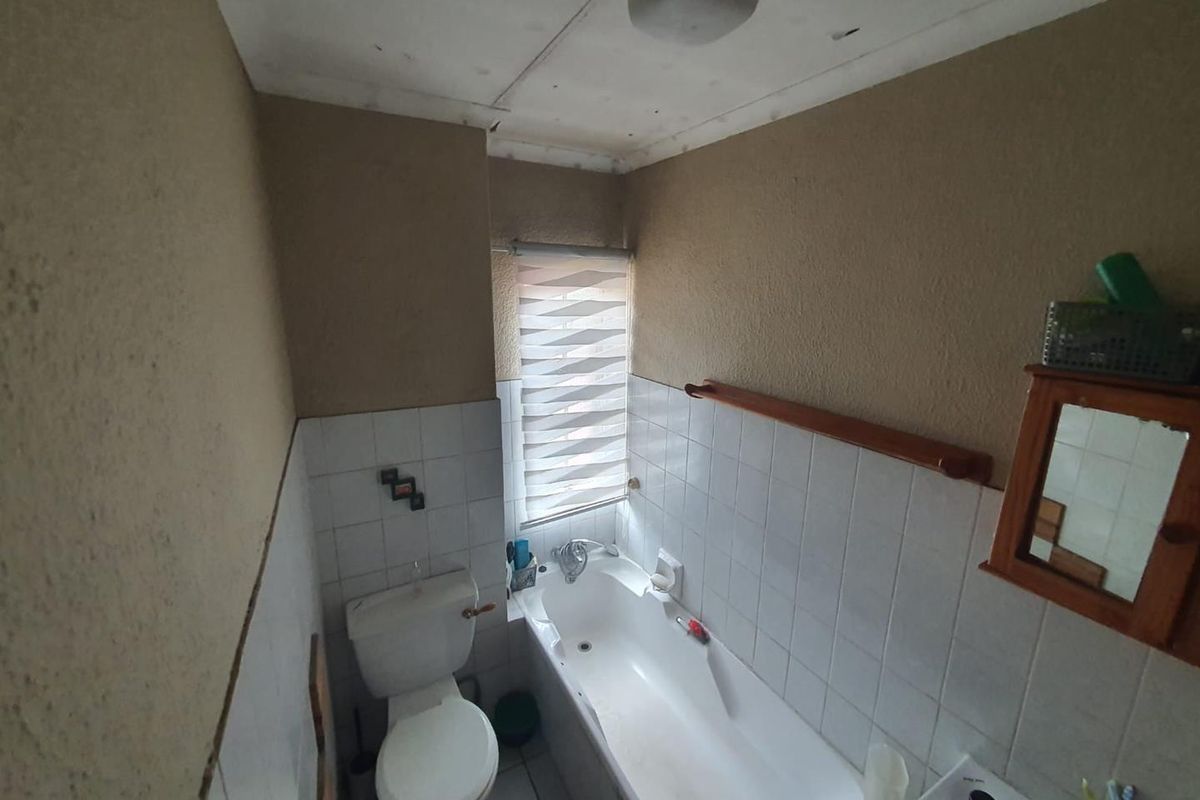 A compact bathroom featuring a standard bathtub, toilet, and wall-mounted basin with dated finishes and textured wall surfaces.