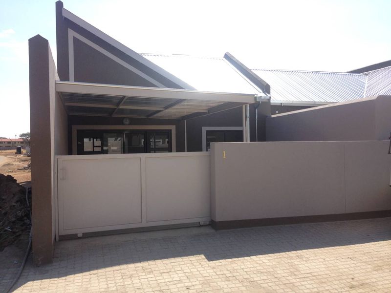 Front elevation of the apartment featuring a paved driveway, secure sliding gate, and a covered carport area.
