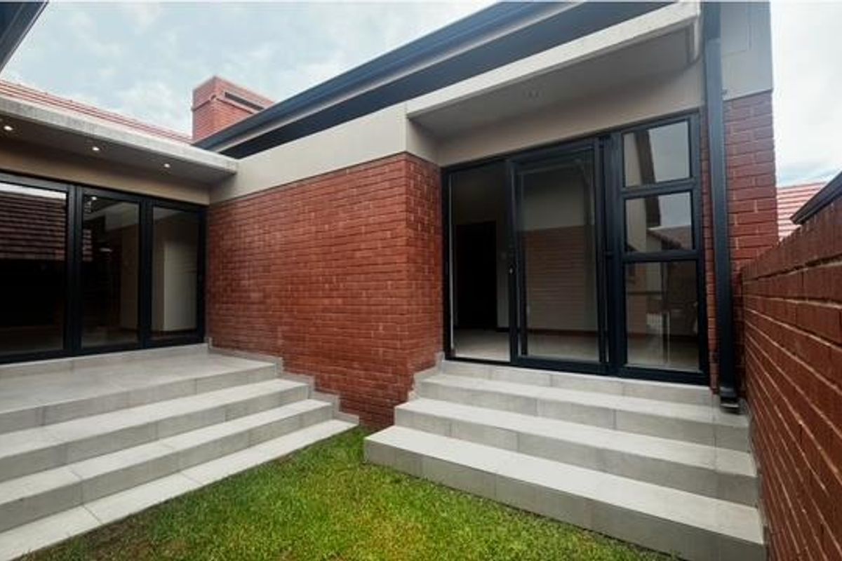A private rear courtyard featuring red brick walls, tiled steps, and modern black-framed glass sliding doors leading into the residence.