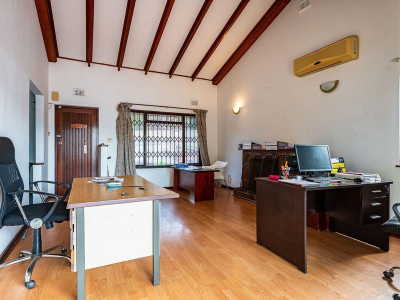 Spacious home office featuring high vaulted ceilings with exposed timber beams, laminate flooring, and a wall-mounted air conditioning unit.