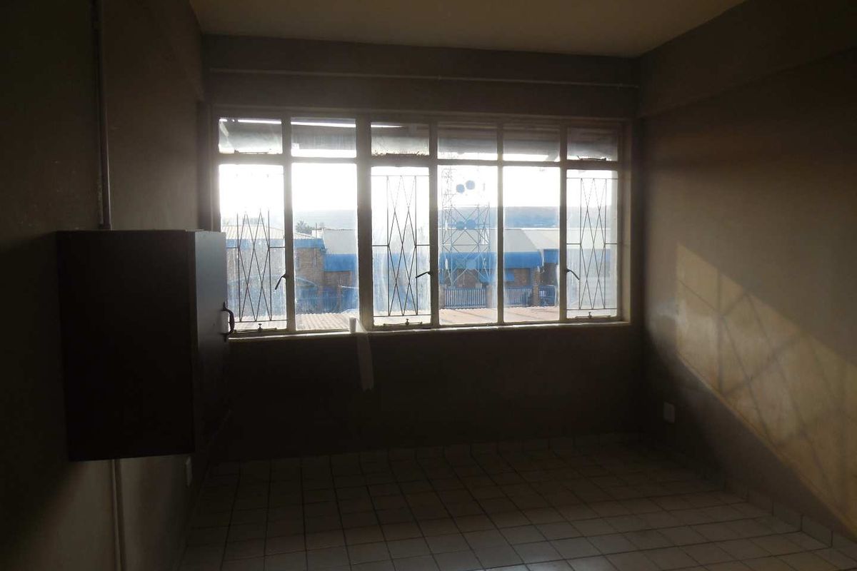 An empty bedroom featuring tiled flooring, security bars on the windows, and a wall-mounted electrical distribution board.