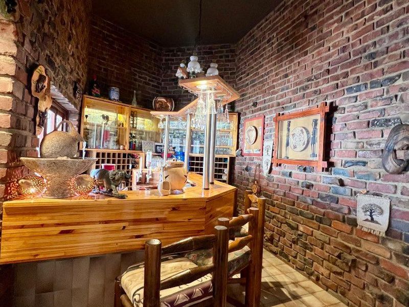 A rustic home bar area featuring exposed brick walls, a built-in wooden bar counter, and integrated glass display cabinetry.