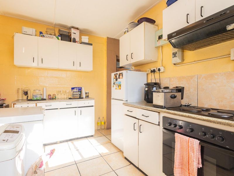 A functional kitchen featuring white built-in cabinetry, laminate countertops, an integrated electric stove with extractor fan, and tiled flooring.
