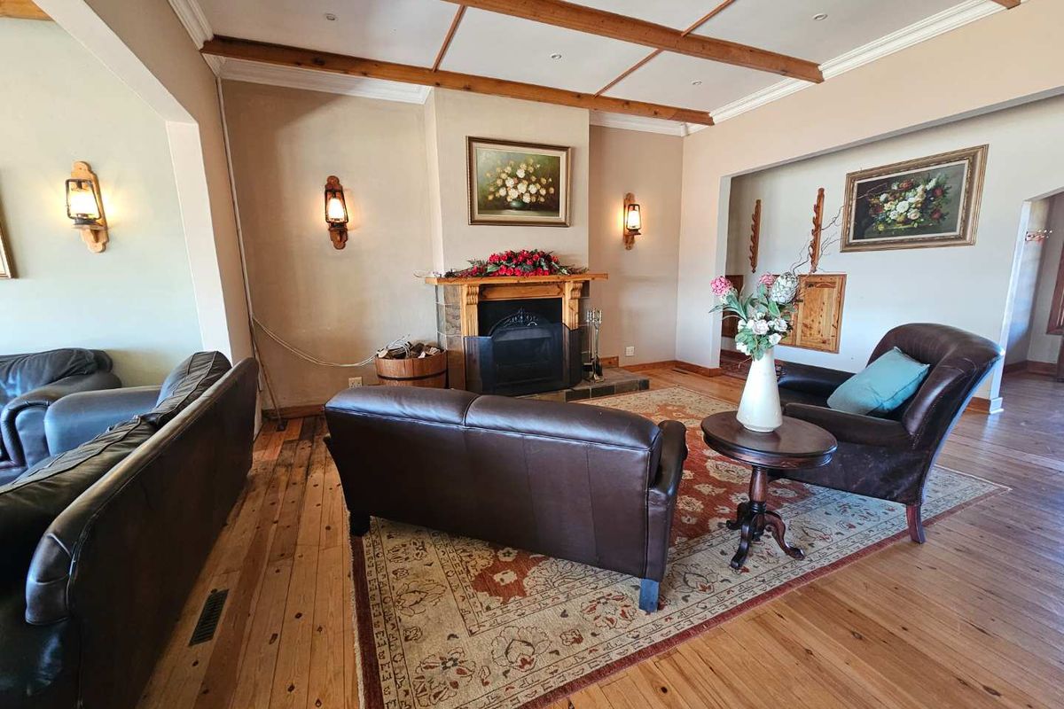 Spacious living room featuring a central fireplace, exposed timber ceiling beams, and warm hardwood flooring, creating a cozy and traditional atmosphere.