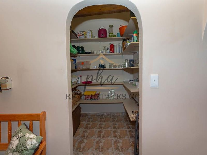 A functional walk-in pantry or scullery area featuring built-in shelving and tiled flooring, accessed through a classic arched doorway.