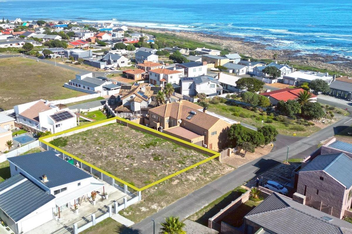 An aerial view of a vacant residential plot in a coastal neighborhood, highlighted with a yellow boundary line, ready for development.