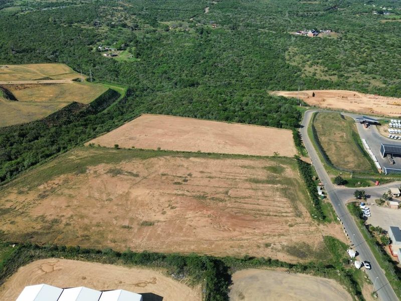 Aerial view of a large, cleared industrial land parcel adjacent to an existing industrial park and access road.