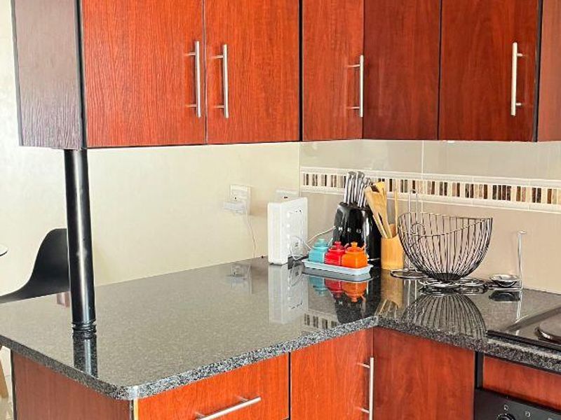 A compact kitchen featuring dark wood-look cabinetry, granite countertops, a built-in oven, and a tiled backsplash.