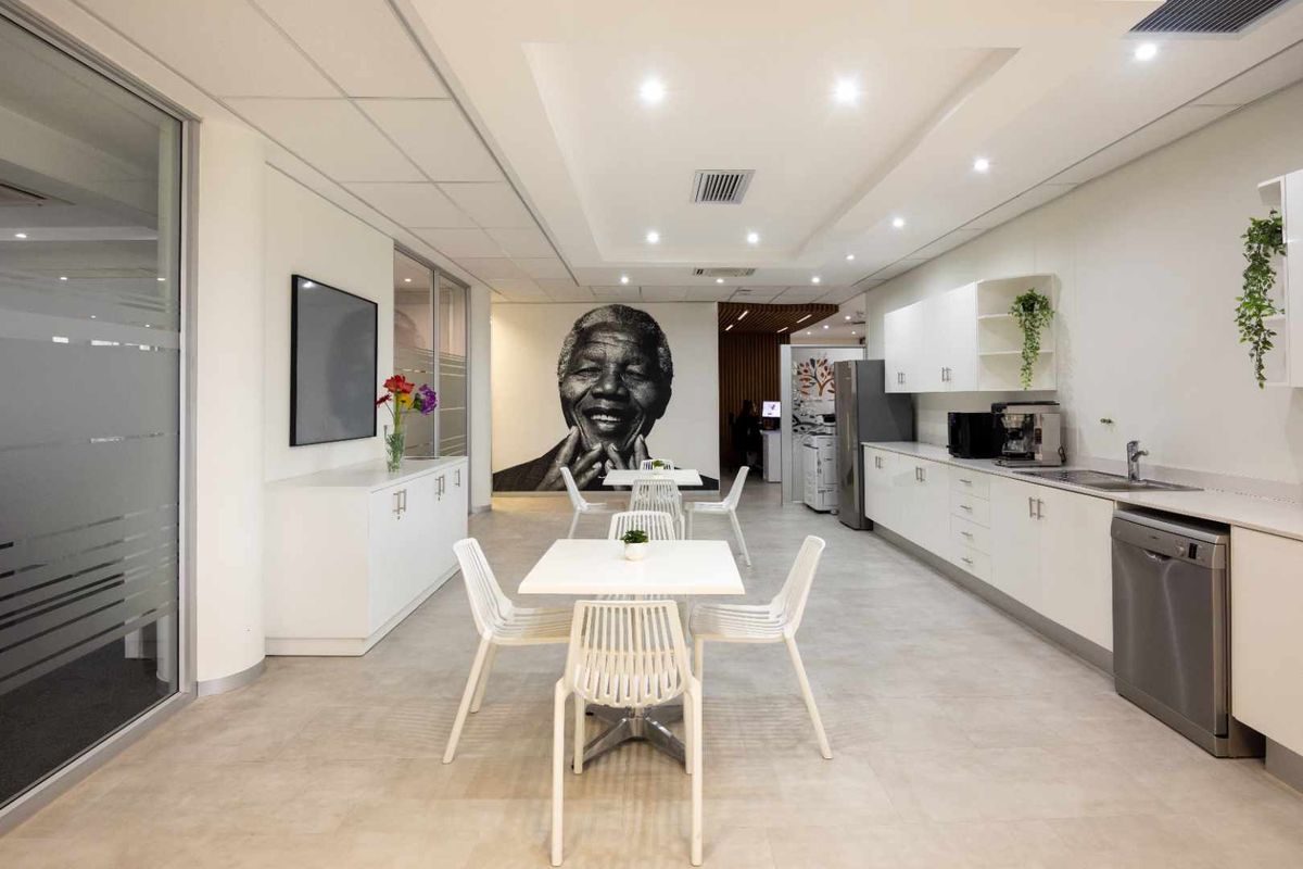 Modern office breakroom featuring a kitchenette with built-in cabinetry, stainless steel sink, and integrated dishwasher, complemented by recessed ceiling lighting.