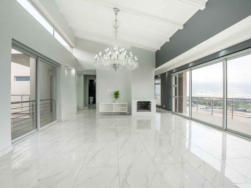 Spacious, light-filled living area featuring high vaulted ceilings, polished marble-look floor tiles, a built-in fireplace, and expansive sliding glass doors with panoramic views.