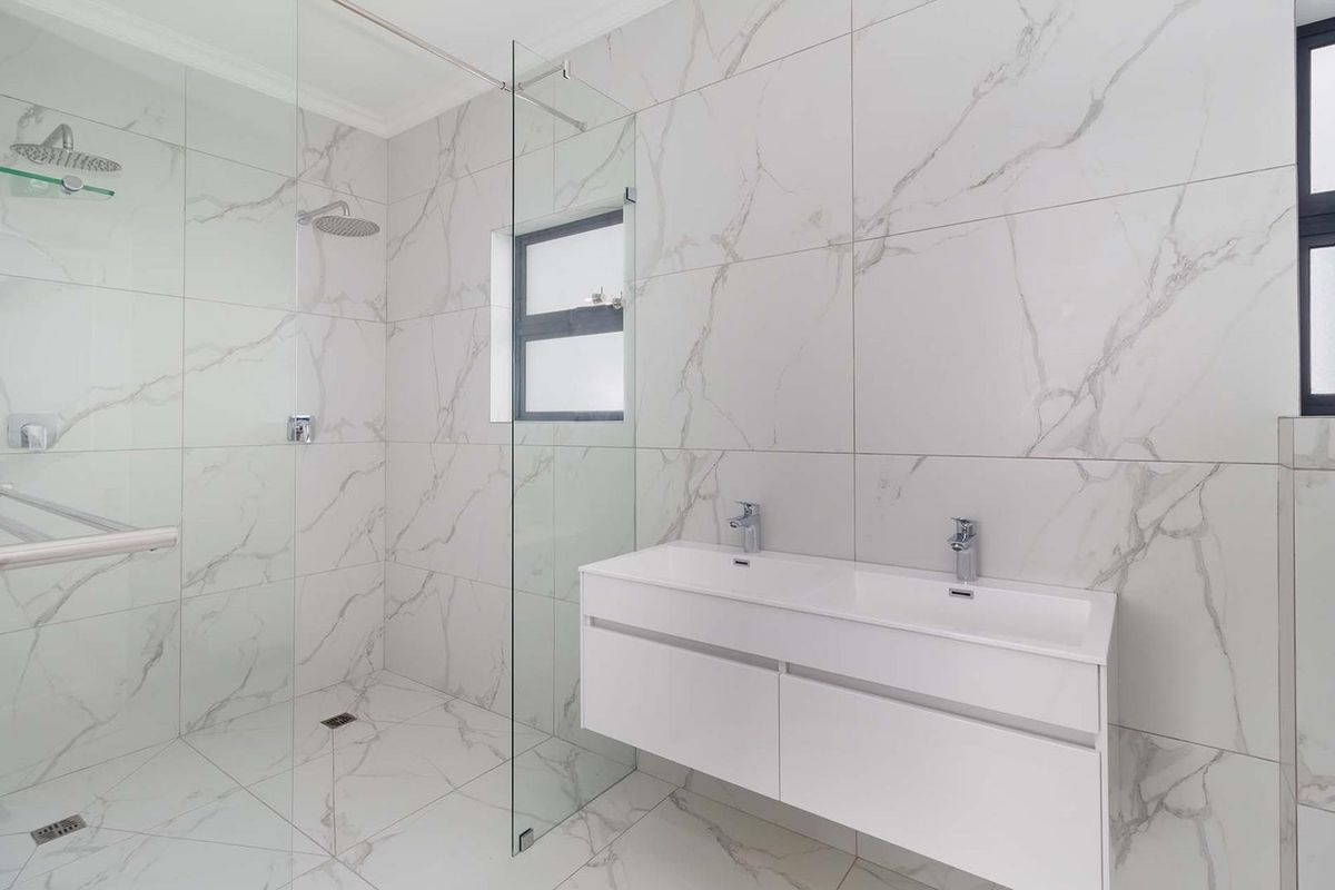 Modern bathroom featuring a spacious walk-in shower with glass screen, double vanity with chrome fixtures, and elegant marble-look floor-to-ceiling tiling.