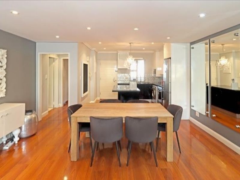 Spacious open-plan living and dining area featuring polished hardwood floors, recessed lighting, and a modern kitchen with a central island and mirrored wall accents.