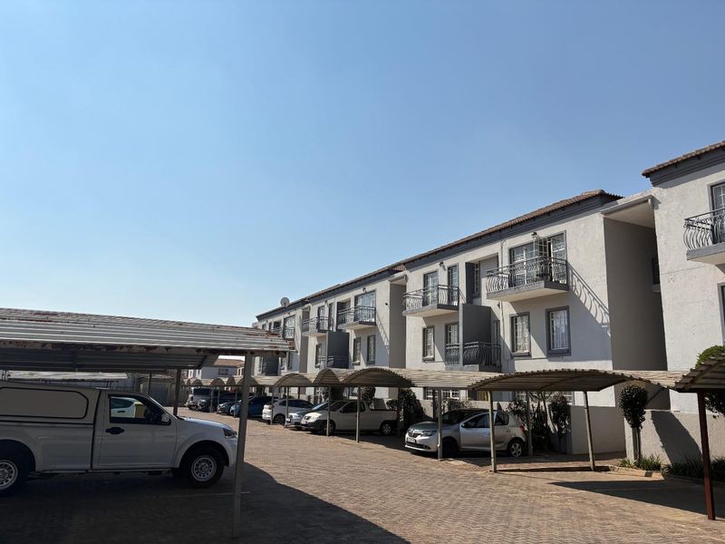 Exterior view of an apartment complex featuring paved parking areas with covered carports and balconies on the upper levels.