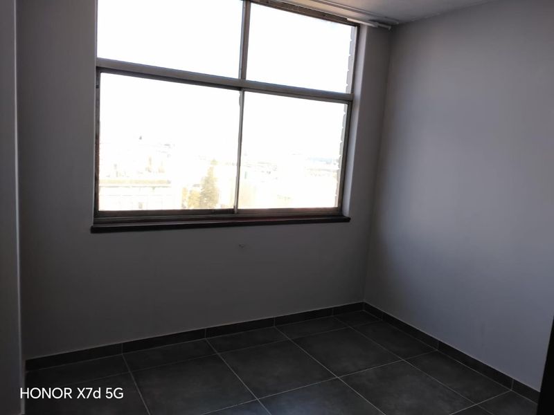 An empty bedroom featuring large windows providing natural light and neutral tiled flooring, ready for personalization.