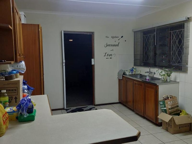 A functional kitchen featuring wooden cabinetry, laminate countertops, a double basin sink, and tiled flooring, offering a practical layout for daily use.
