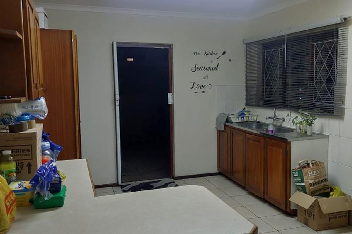 A functional kitchen featuring wooden cabinetry, laminate countertops, a double basin sink, and tiled flooring, offering a practical layout for daily use.