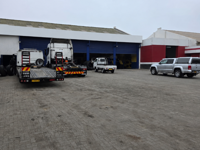 Industrial property exterior featuring a large paved yard and multiple roller shutter access doors for commercial or logistics operations.