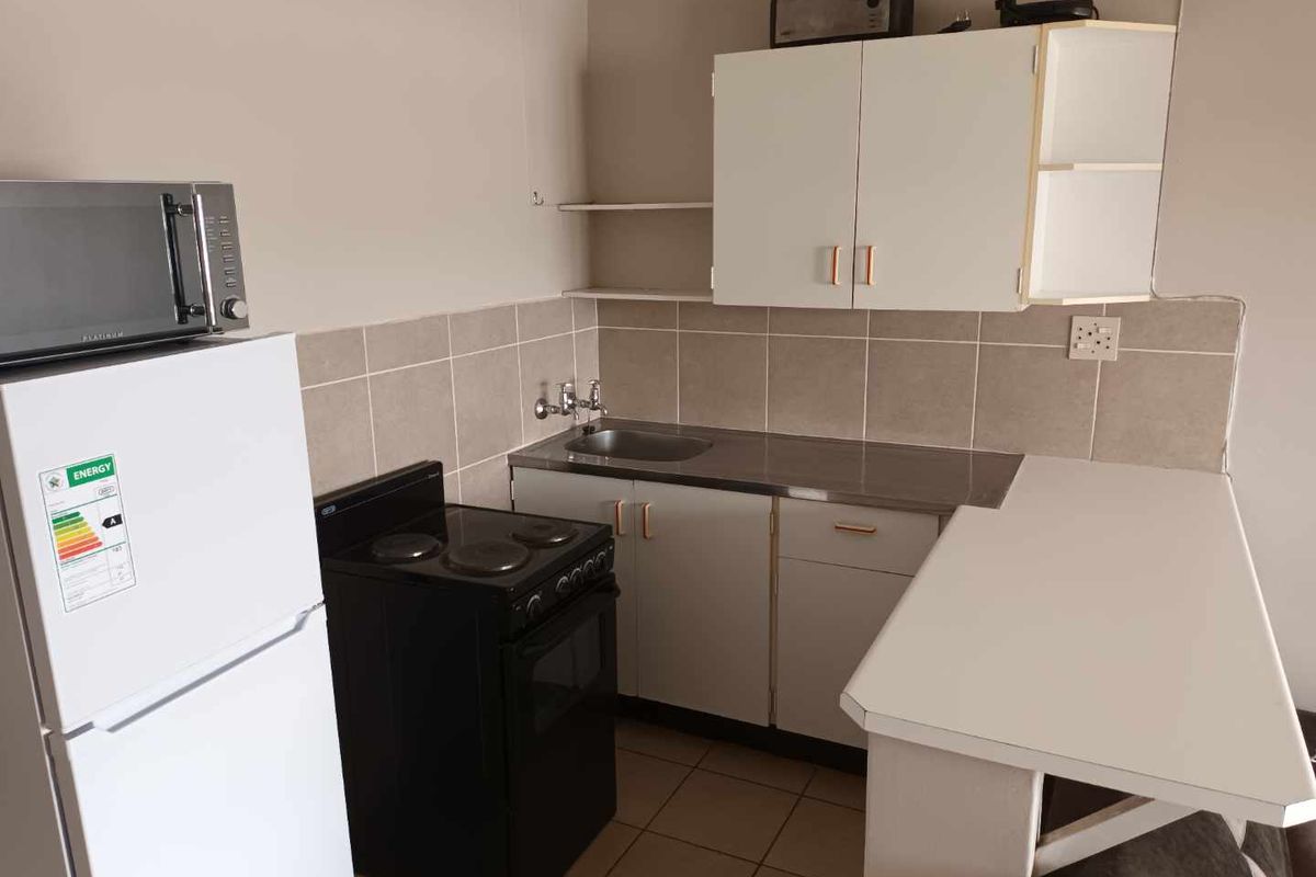 Compact kitchen featuring built-in cabinetry, a stainless steel sink, tiled backsplash, and an integrated breakfast bar, offering a functional layout for an apartment.