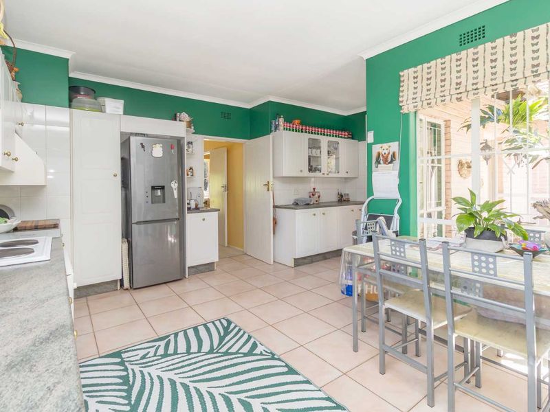 A functional kitchen featuring white cabinetry, tiled flooring, and a built-in hob, with direct access to an adjacent room and natural light from windows.