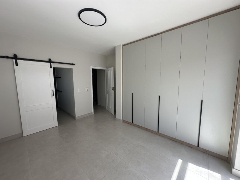 A modern, spacious bedroom featuring neutral tiled flooring, extensive built-in cabinetry, and a stylish sliding barn door leading to an adjacent space.