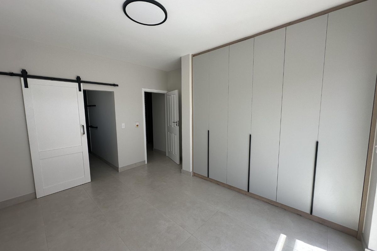 A modern, spacious bedroom featuring neutral tiled flooring, extensive built-in cabinetry, and a stylish sliding barn door leading to an adjacent space.