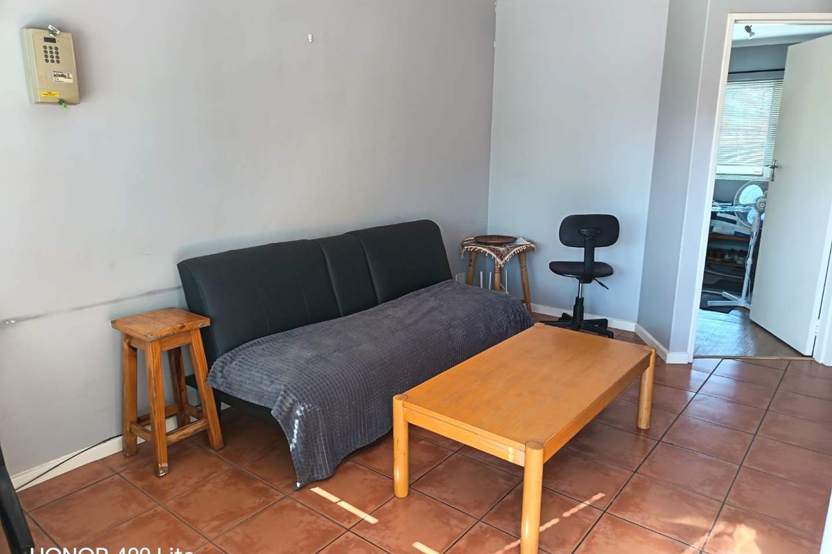 A living room area featuring terracotta floor tiles and neutral grey walls, providing a functional space with direct access to an adjacent room.