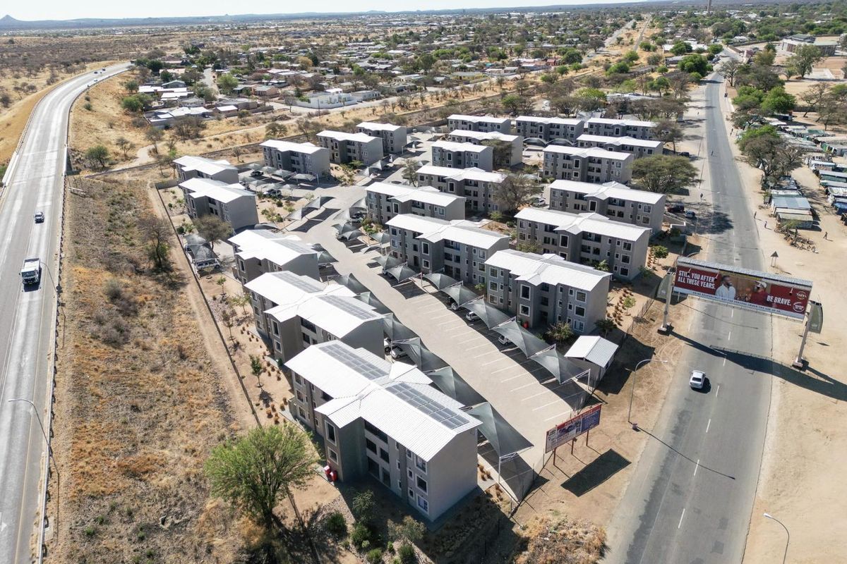 Aerial view of a modern apartment complex featuring multiple residential blocks, paved parking areas with shade ports, and solar panel installations.