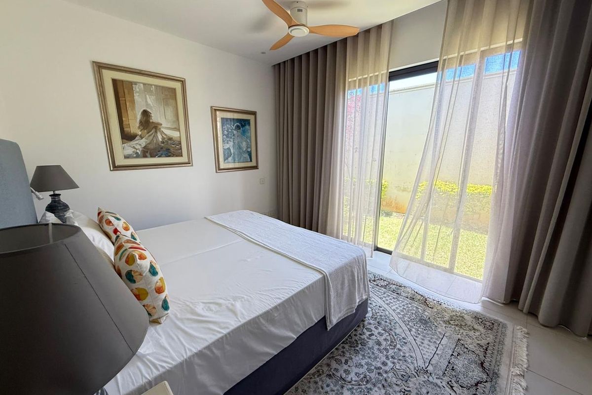 A bright bedroom featuring a ceiling fan, tiled flooring, and large sliding glass doors that provide direct access to the garden.