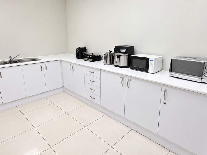 A clean and functional office kitchenette featuring white cabinetry, laminate countertops, a double sink, and tiled flooring.