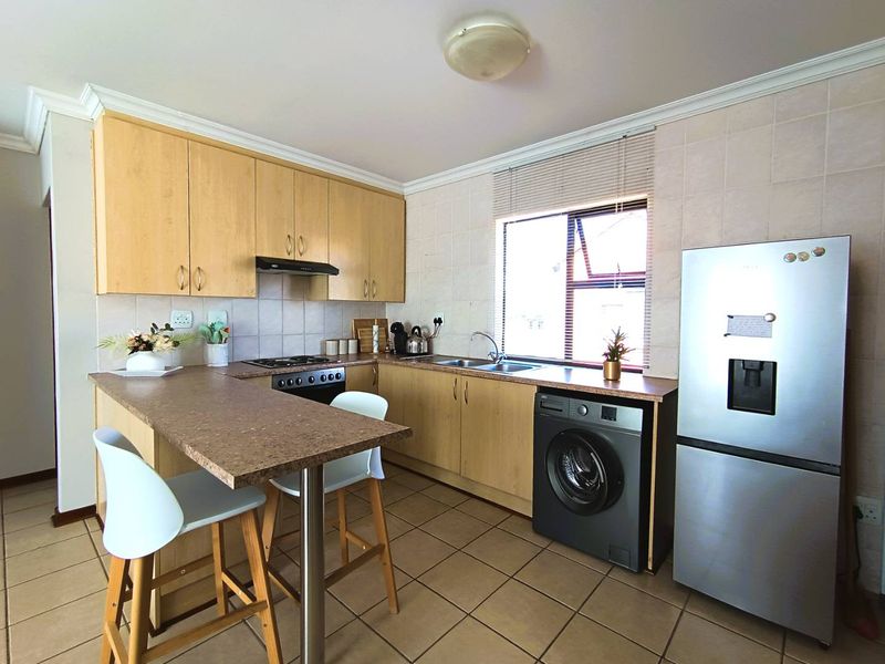 Functional kitchen featuring light wood cabinetry, laminate countertops, a breakfast bar, gas hob, and tiled finishes throughout.