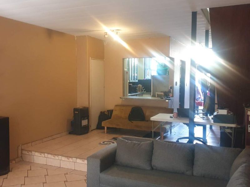 Open plan living area featuring tiled flooring, a raised platform section, and a kitchen pass-through window, offering potential for modern renovation.