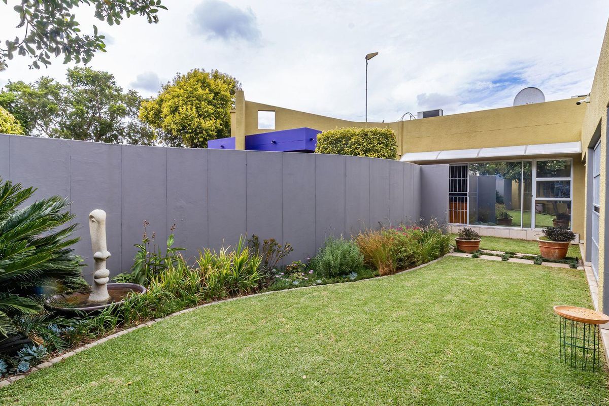 A well-maintained private rear garden area featuring a manicured lawn, landscaped garden beds, and a perimeter boundary wall.