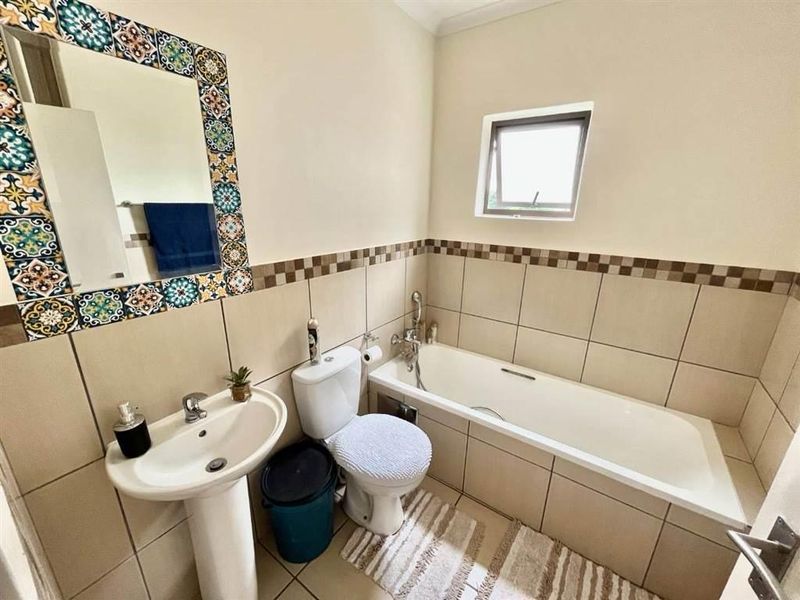 A functional bathroom featuring a pedestal basin, a built-in bathtub, and decorative tiled wall accents, providing a practical space with neutral finishes.